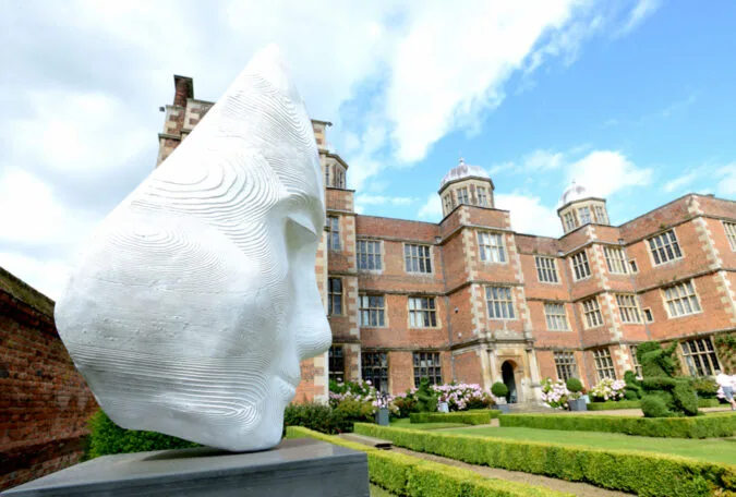 White stone face sculpture with Doddington Hall in the background