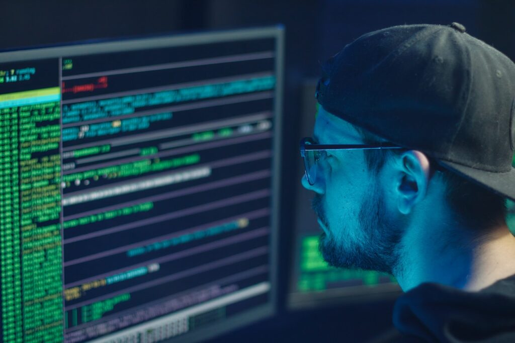 Sneaky digital spy or hacker looking at super secret code. You can tell he's up to no good because he's in a dark room and has his hat on backwards. Photo by Mikhail Nilov, Pexels